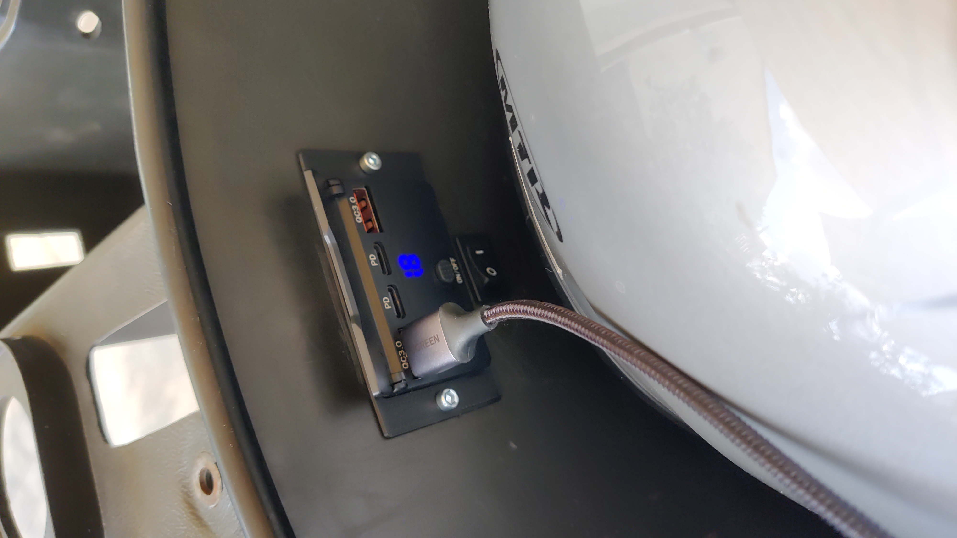 Ein Helm liegt im Helmfach und an der aufgeklappten USB-Steckdose hängt ein Kabel.