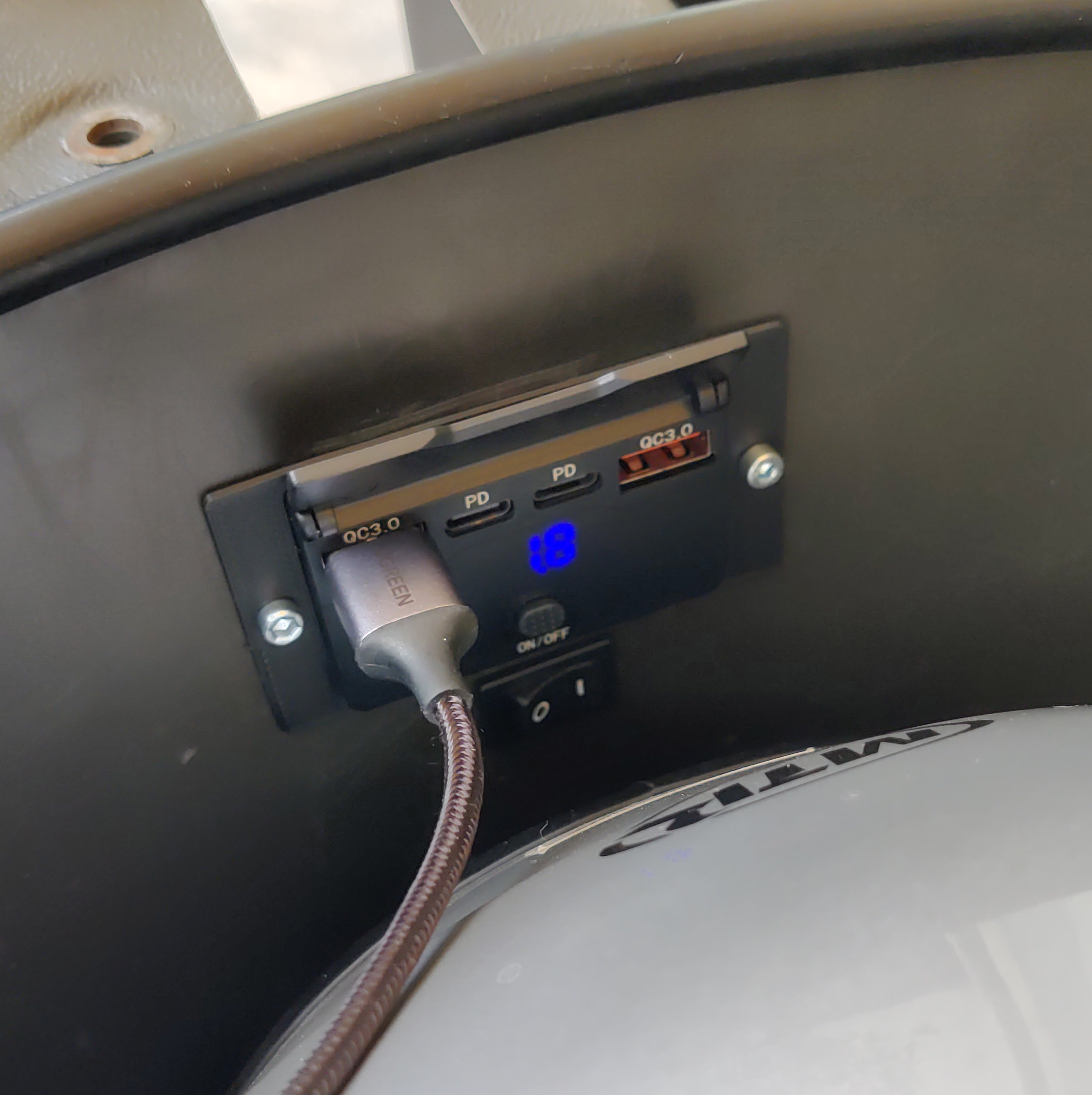 Ein Helm liegt im Helmfach und an der aufgeklappten USB-Steckdose hängt ein Kabel.
